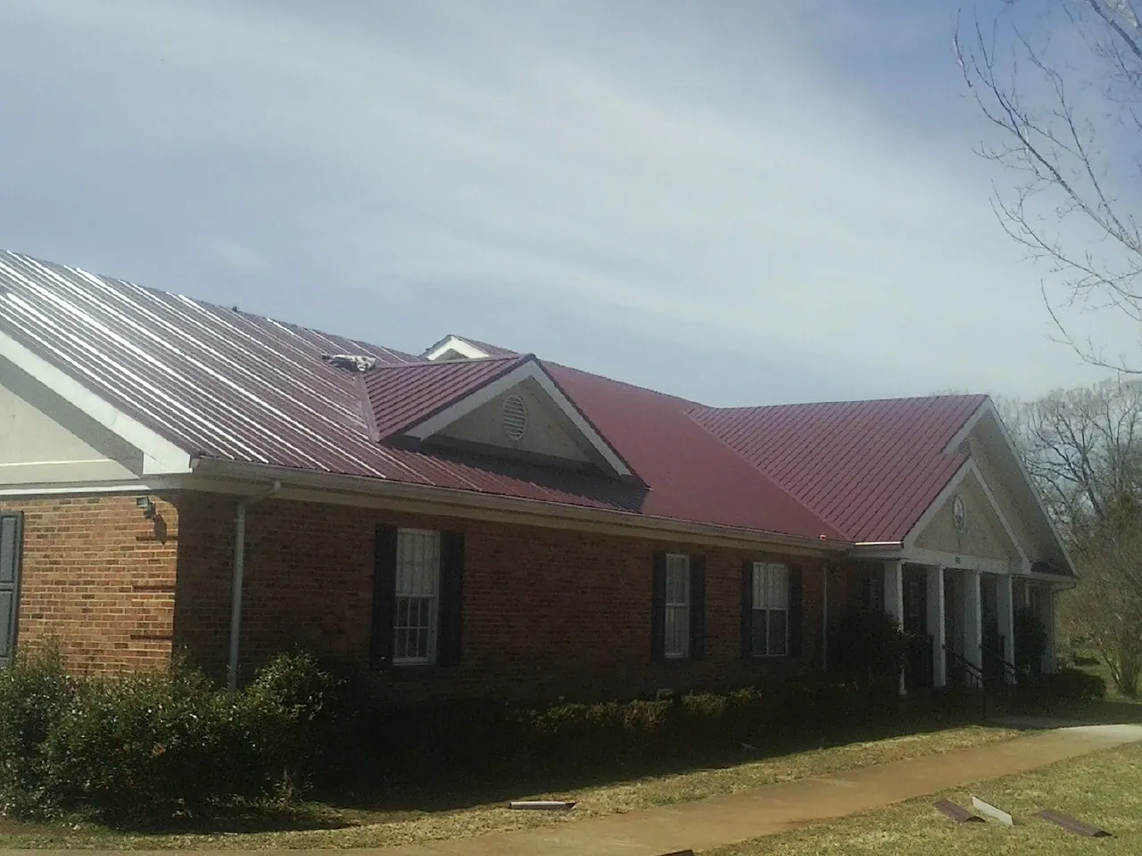Red metal roof with gabled entries on a long brick building, from a Hail Damage Roof Repair job in Jamison