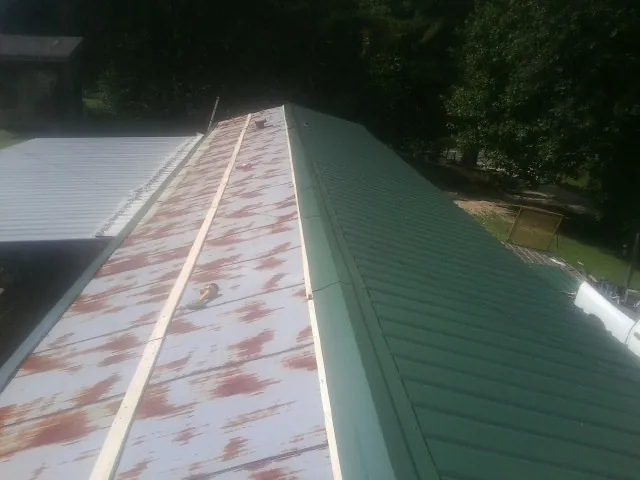Old rusted panels beside newly installed green metal roofing — Wind Damage Roof Repair by Roofing Brothers in Jamison