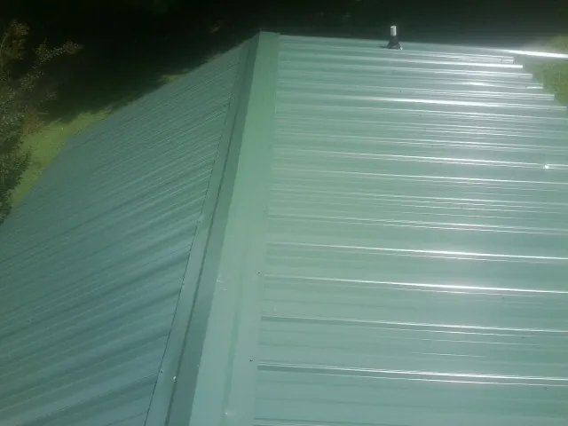 New green metal panels meeting at the ridge of a roof — Flat Roof Repair work by our crew in Jamison