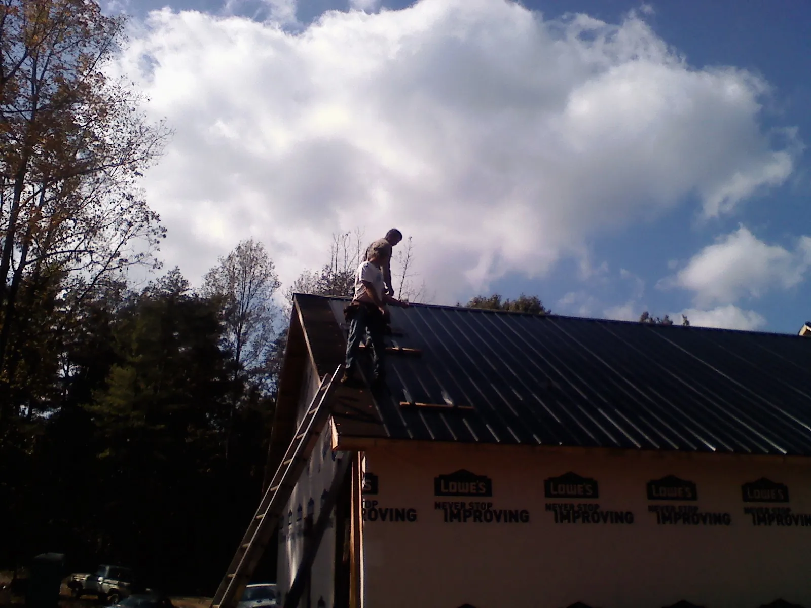 Roofer fastening dark metal panels high against a cloudy sky, from a Roof Inspection job in Jamison